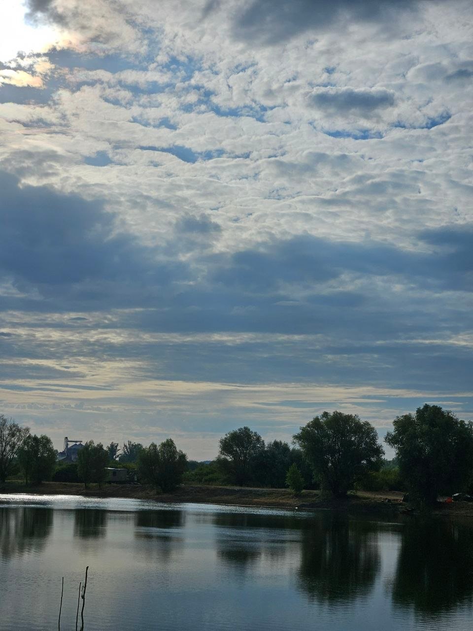 A wide sky of fleecy clouds over Lake Provala, trees reflected in the water
