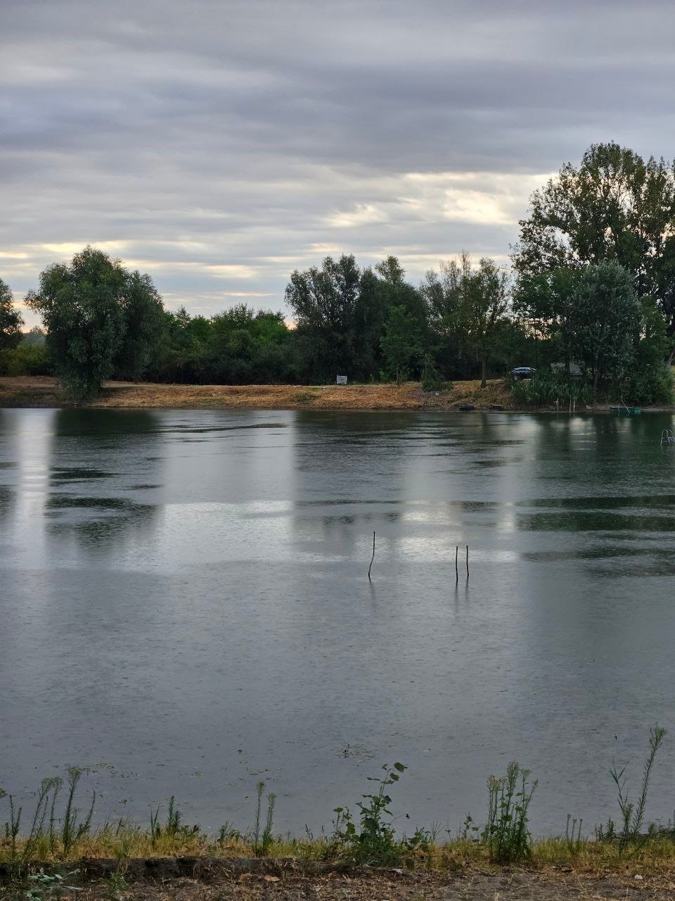 Rain on Lake Provala under a grey sky, fishing rod rests standing in the water