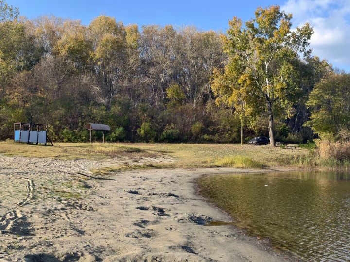 The sandy beach of Lake Provala in autumn: changing cabins, a shade roof and the forest behind