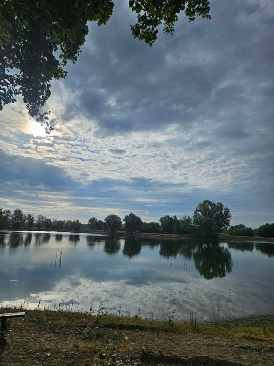 The sun behind clouds over Lake Provala, the sky and trees mirrored in the lake